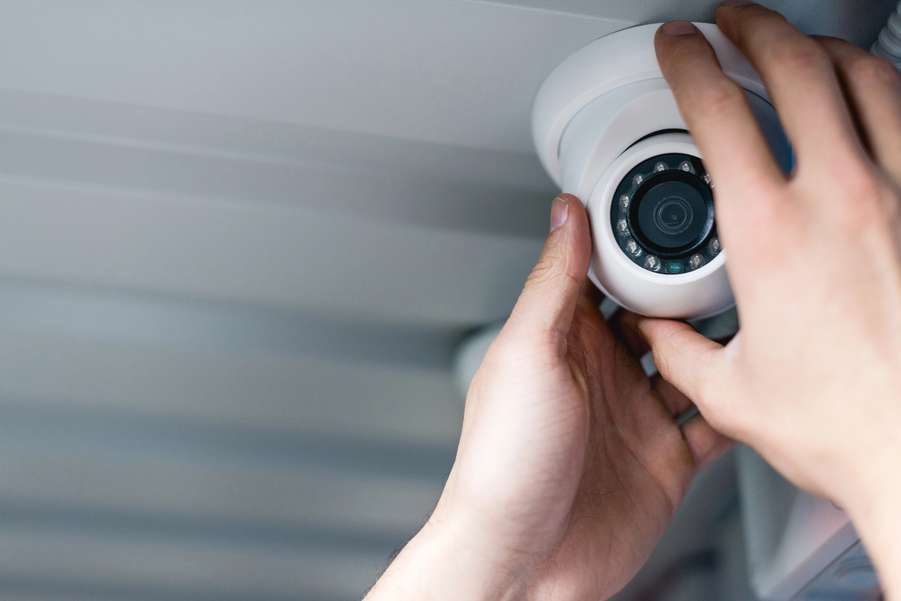 Technician installing a dome-style security camera on a ceiling, adjusting the camera lens by hand.