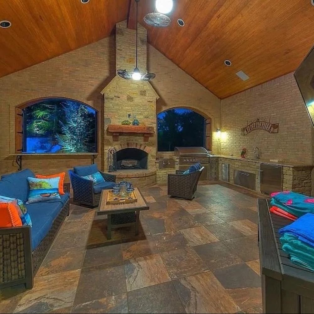 covered patio with a wood ceiling, brick fireplace, custom outdoor kitchen, seating, and integrated TV.