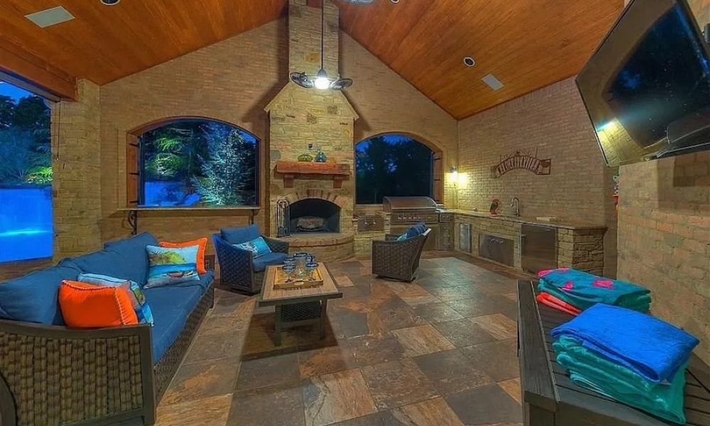 covered patio with a wood ceiling, brick fireplace, custom outdoor kitchen, seating, and integrated TV.